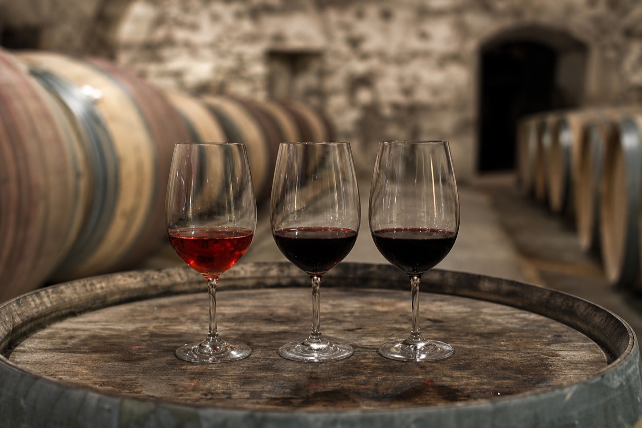 Two glasses of red wine side by side on a barrel, one deeper and darker than the other